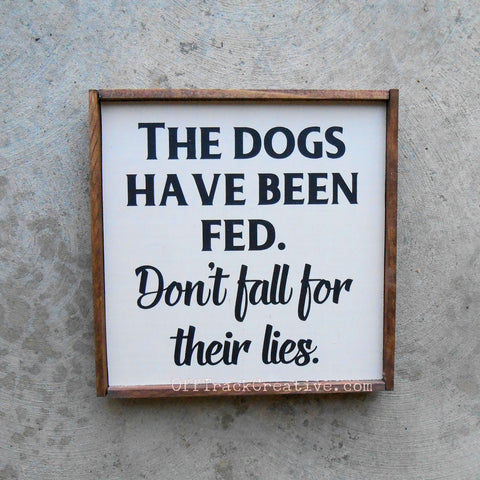 Painted wood sign that says The Dogs have been fed. Don't fall for their lies.