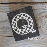 Block of wood with painted on checkered letter Q.