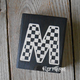 Block of wood with painted on checkered letter M.