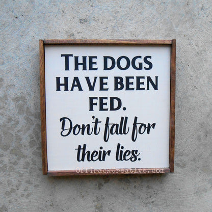 Painted wood sign that says The Dogs have been fed. Don't fall for their lies.